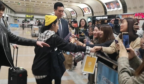 10月19日，在北京首都机场，韩国人气歌手IU（戴黄帽子）抵达机场后同粉丝握手。（韩联社）