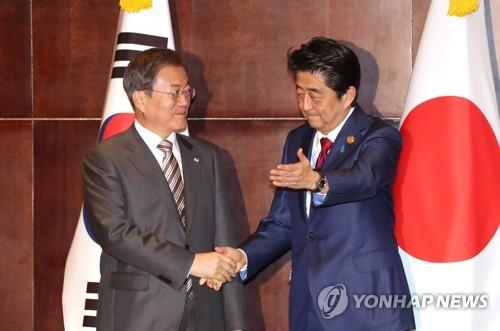 12月24日，在成都，韩国总统文在寅（左）和日本首相安倍晋三握手合影。 韩联社