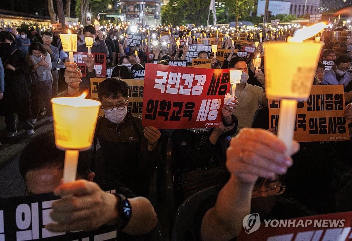 资料图片：5月30日，在首尔中区德寿宫大汉门前，大韩医师协会的成员们手举"医学院扩招宣告韩国医疗死亡"等标语举行烛光集会，抗议政府推进扩招计划。 韩联社