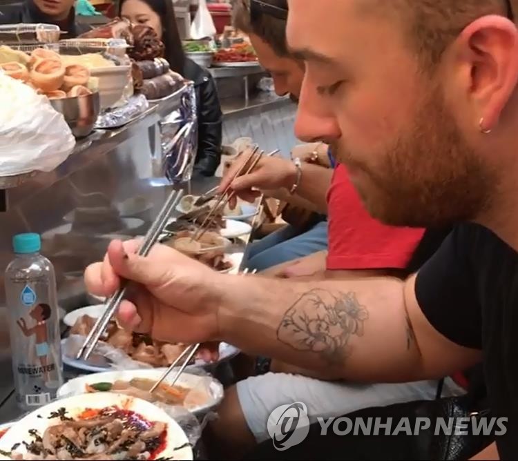 资料图片:今年10月,在首尔广藏市场,访韩的英国著名歌手萨姆·史密斯品尝活章鱼。(SNS截图)