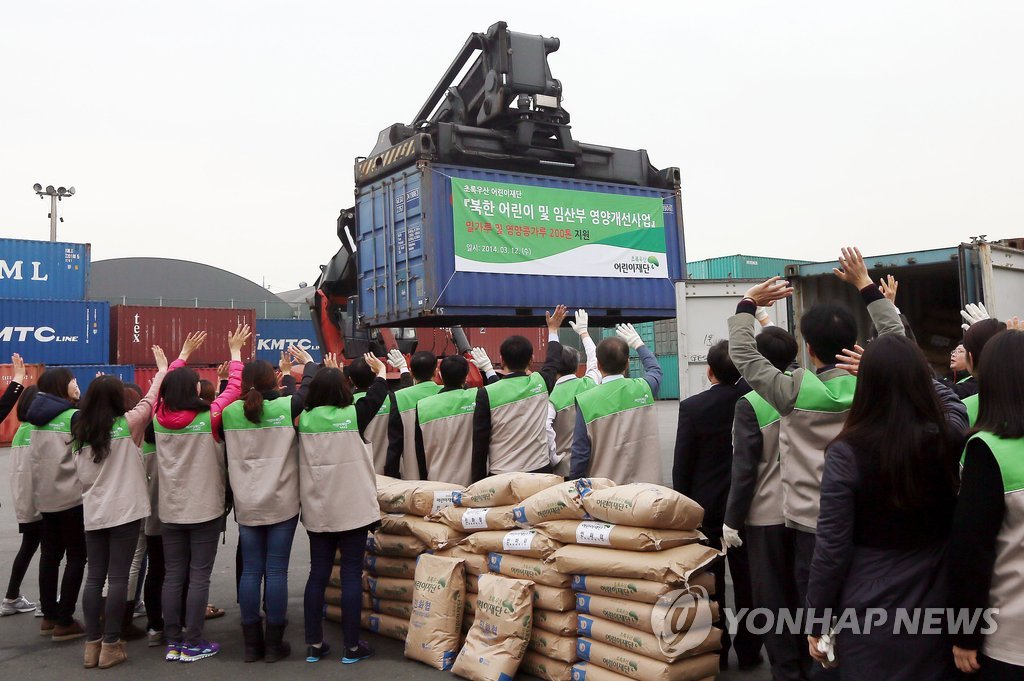 资料图片：2014年3月12日，在仁川，韩国绿伞儿童基金会的志愿者向装载该组织为朝鲜弱势群体提供的援助物资的集装箱挥手致意。 韩联社