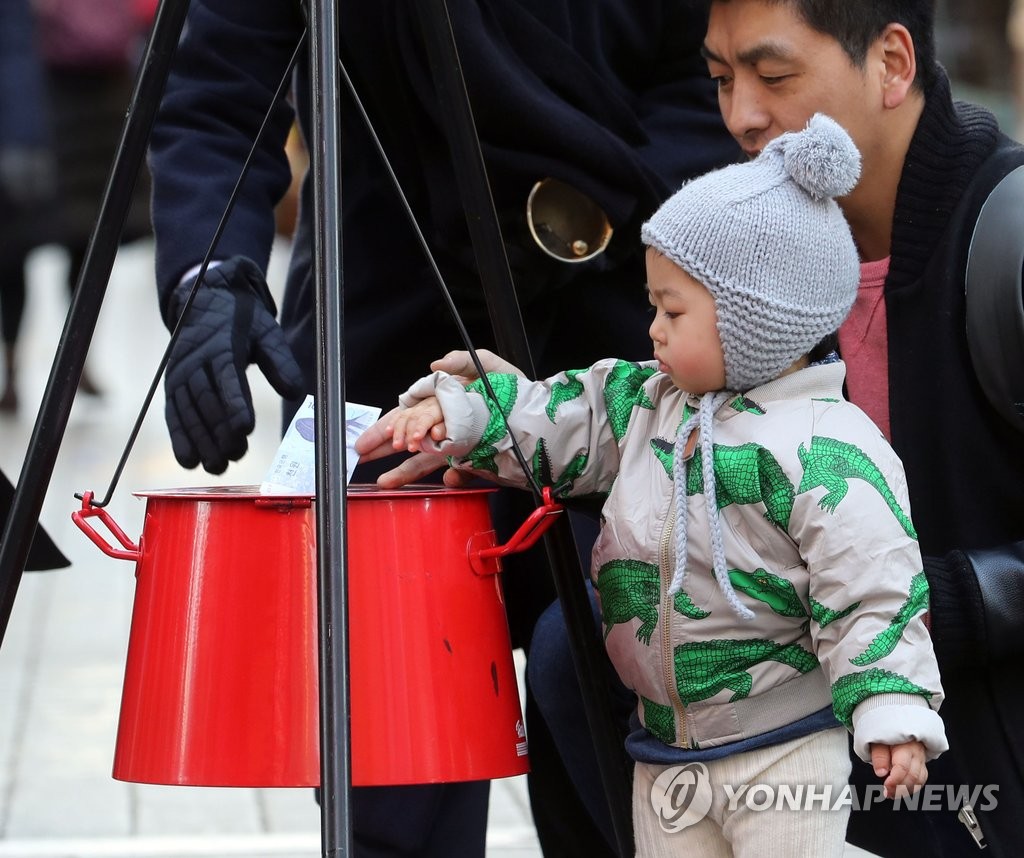 资料图片：2016年12月，在首尔明洞大街，一名小朋友在爸爸的陪伴下向救世军“慈善锅”捐款。（韩联社）