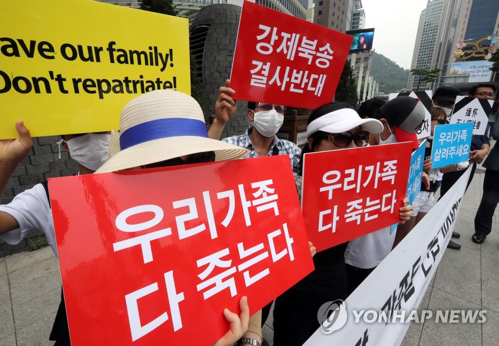 资料图片：2017年8月，在中国驻韩国大使馆前，脱北者及其家属举牌抗议中国政府强制遣返脱北者的行为。 韩联社