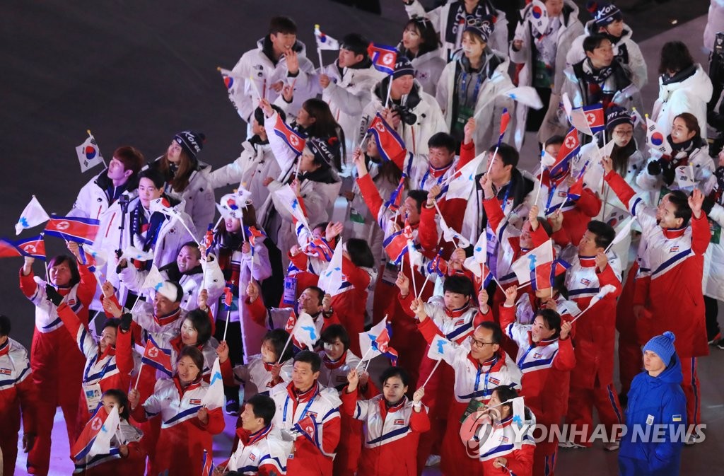 2月25日，在江原道平昌奥林匹克体育场，手举太极旗、人工旗和韩半岛旗的韩朝运动员们打成一片亮相平昌冬奥闭幕式。(韩联社)