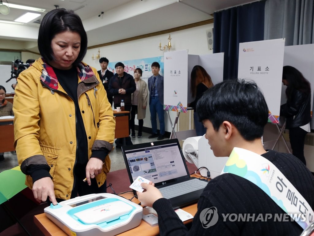 资料图片：2018年4月16日，一名外国移民（左）正在参加缺席投票体验活动。 韩联社
