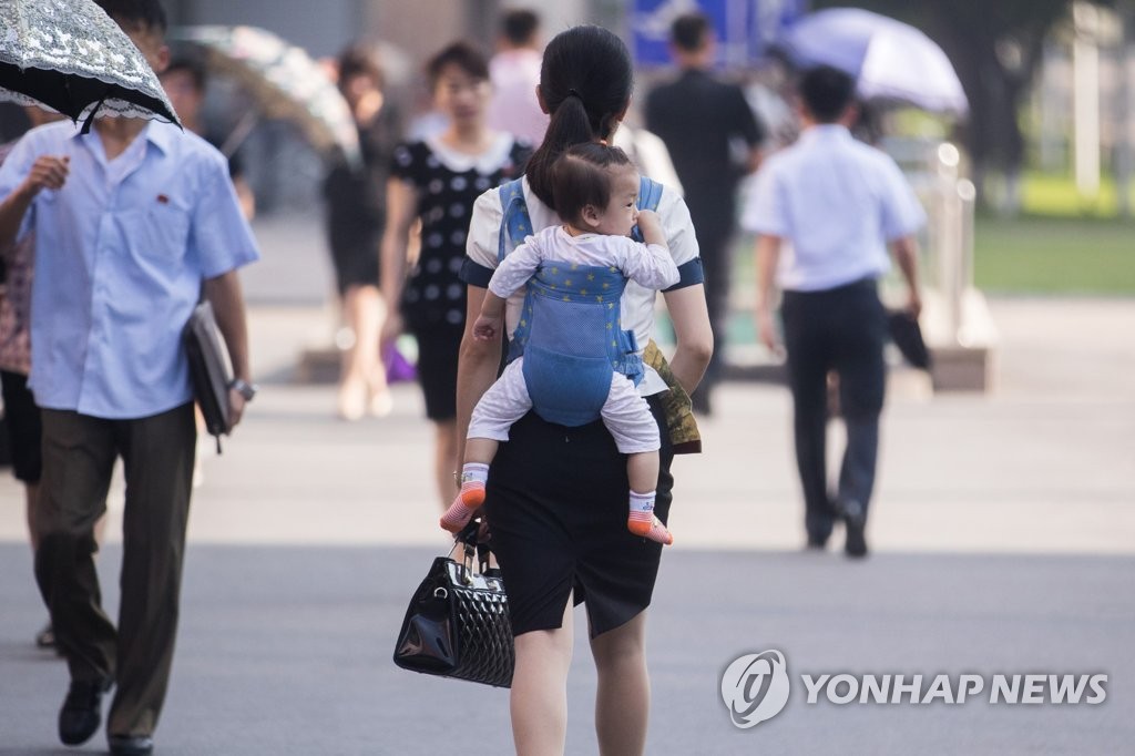 资料图片：2018年7月4日上午，在平壤街头，一位身着西装的女士背着孩子走在街头。 韩联社/韩媒摄影记者团供图（图片严禁转载复制）