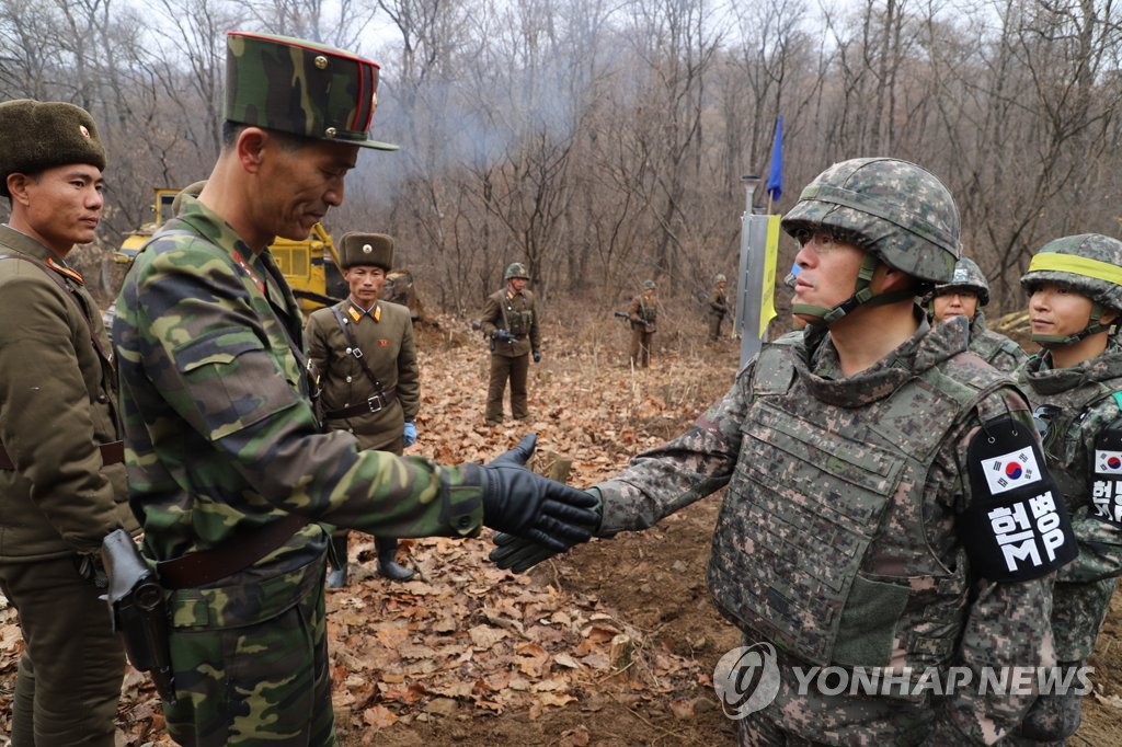 资料图片：2018年11月22日，在非军事区，韩朝为共同挖掘遗骸修建道路的人员握手致意。（韩联社/国防部供图）