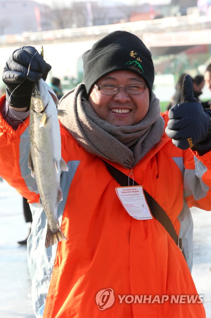 资料图片：1月20日，在江原道华川，参加山鳟鱼庆典的一名游客手举山鳟鱼拍照留念。（韩联社）