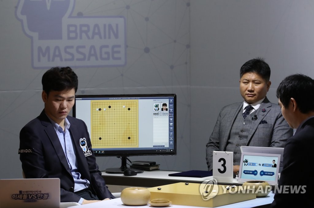 12月18日,在按摩椅厂商Bodyfriend总部,研发人工智能围棋程序“韩豆”的NHN公司员工李和燮(音译)与李世石对坐(右)替“韩豆”落子。李和燮曾是韩国棋院研究生,棋力达到业务五段水平。 韩联社
