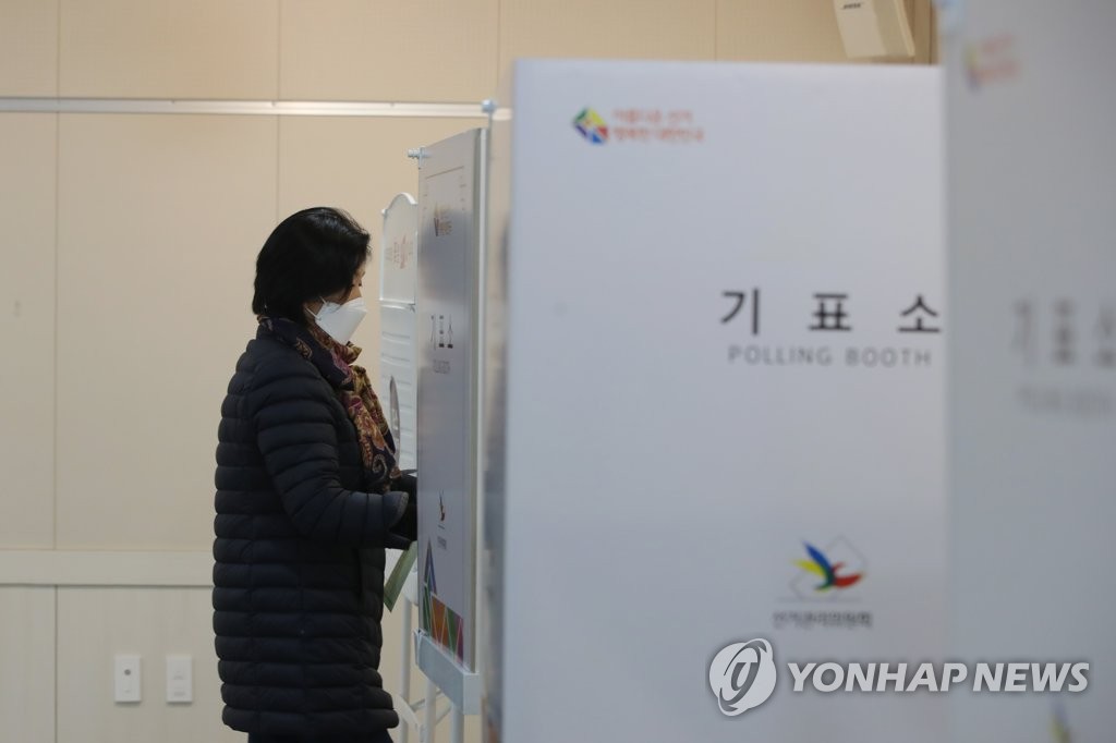 资料图片：4月15日，在光州南区的一投票站，一位选民戴着口罩进入划票间。 韩联社