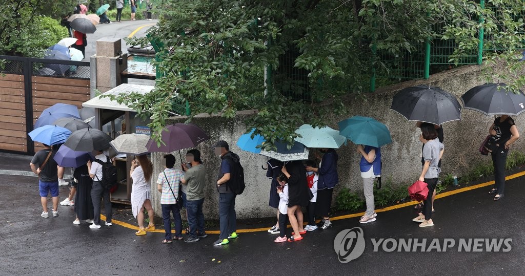 资料图片：人们撑伞在中国驻韩大使馆领事部前排长龙等待办签证，图片摄于8月5日。 韩联社