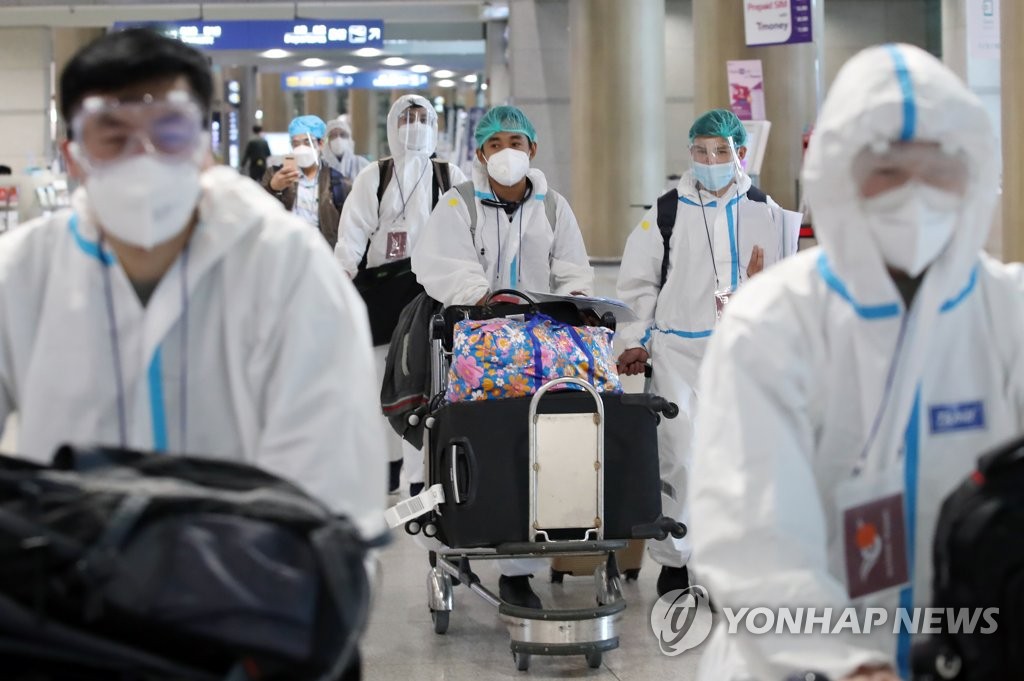 资料图片：入境人员身穿防护服前往临时隔离设施。 韩联社