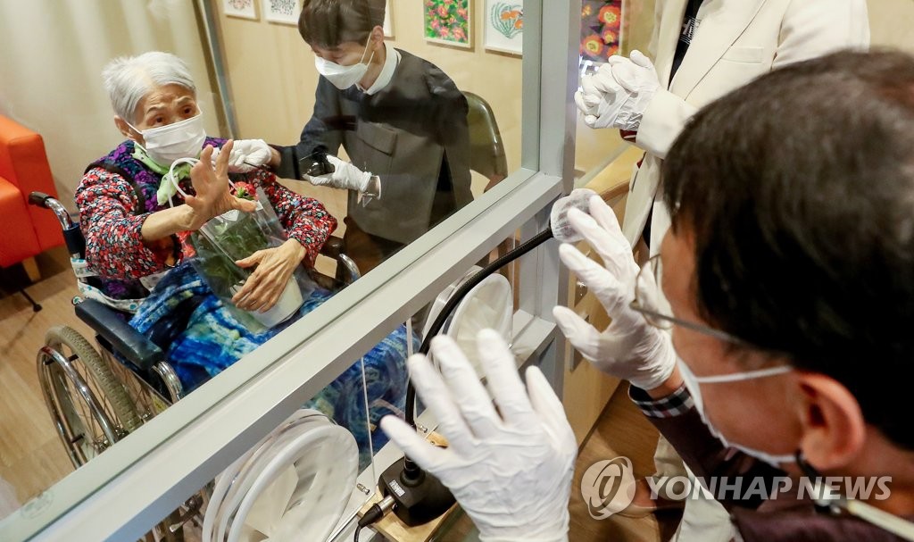 资料图片：5月7日，在首尔市一家疗养设施的探亲室，入住该设施的一位奶奶与前来探访的儿孙对话。 韩联社