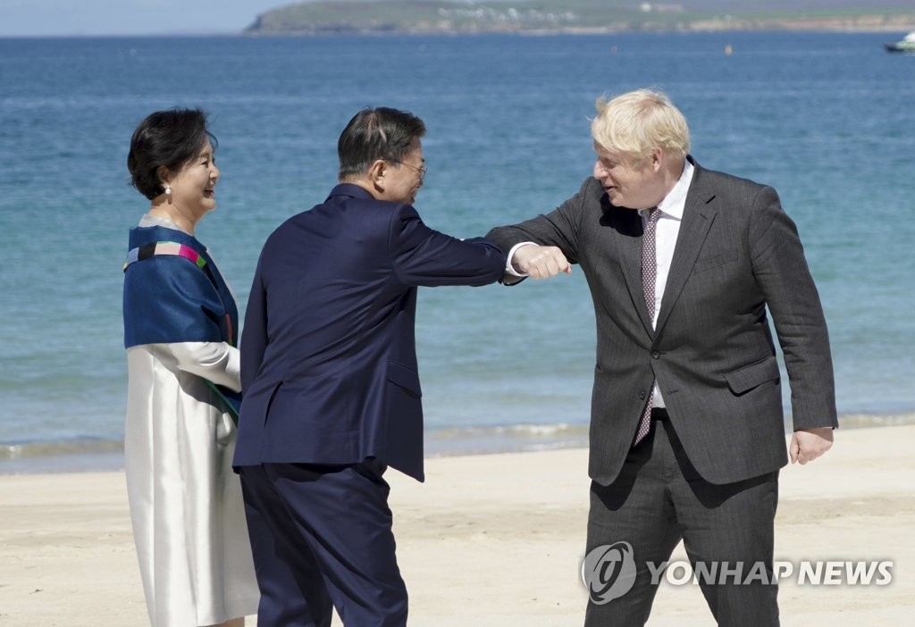 资料图片：当地时间6月12日，在英国康沃尔卡比斯贝，总统文在寅（左二）与夫人金正淑（左一）出席七国集团（G7）峰会受邀国欢迎仪式。图为文在寅（中）与英国首相约翰逊（右）碰肘致意。 韩联社