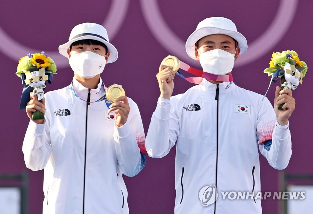 7月24日，在东京梦之岛公园，韩国射箭运动员金济德（右）和安山举起金牌庆祝夺金。在当天下午进行的东京奥运会射箭混合团体决赛上，金济德/安山组合以5比3力压荷兰队，夺得金牌。 韩联社