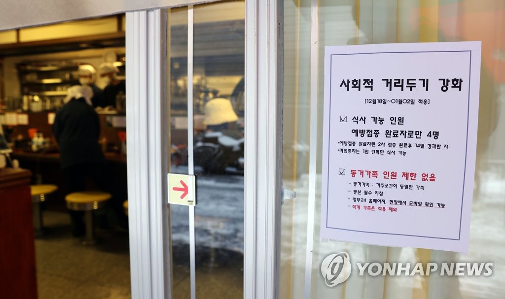 资料图片：一家咖啡厅在门上贴出有关社交距离限制措施的公告。 韩联社