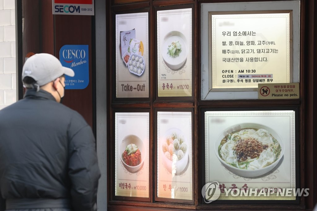 资料图片：一名路人驻足查看一餐馆用餐价格。 韩联社
