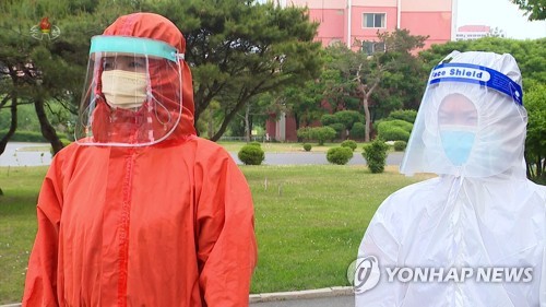 5月19日，朝鲜中央电视台播出身穿隔离服的防疫工作人员画面。站在右侧的大白头戴印有英文“Face Shield”字样的隔离面罩。 韩联社/朝鲜央视（图片仅限韩国国内使用，严禁转载复制）