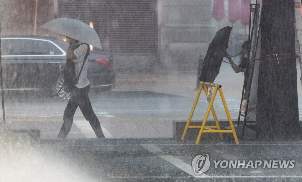 8月8日，在首尔汝矣岛，市民们撑伞顶着暴雨走在下班路上。 韩联社