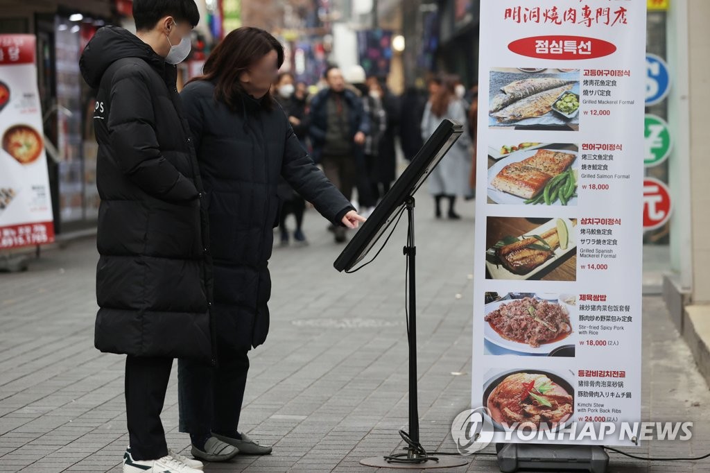 资料图片：在首尔明洞，行人在一家餐厅门口了解菜品。 韩联社