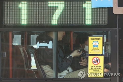 资料图片：3月20日，随着政府解除公共交通工具佩戴口罩义务，一位市民摘下口罩利用公交车。 韩联社