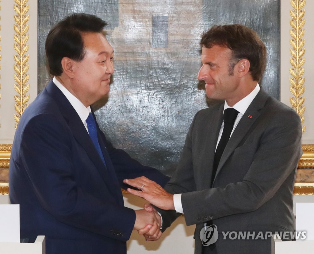 资料图片：当地时间6月20日，在法国巴黎爱丽舍宫，韩国总统尹锡悦（左）和法国总统马克龙在会谈前发表联合声明。图为双方握手致意。 韩联社
