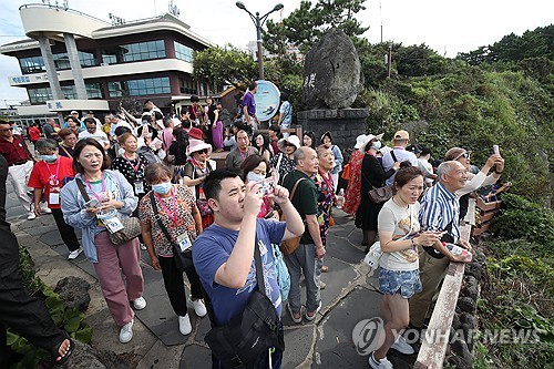 资料图片：8月31日，在济州港，自上海出发的“蓝梦之星”号邮轮（吨位2.4782万吨）靠港停泊。图为中国团体游客观赏济州龙头岩。 韩联社/济州道摄影记者会