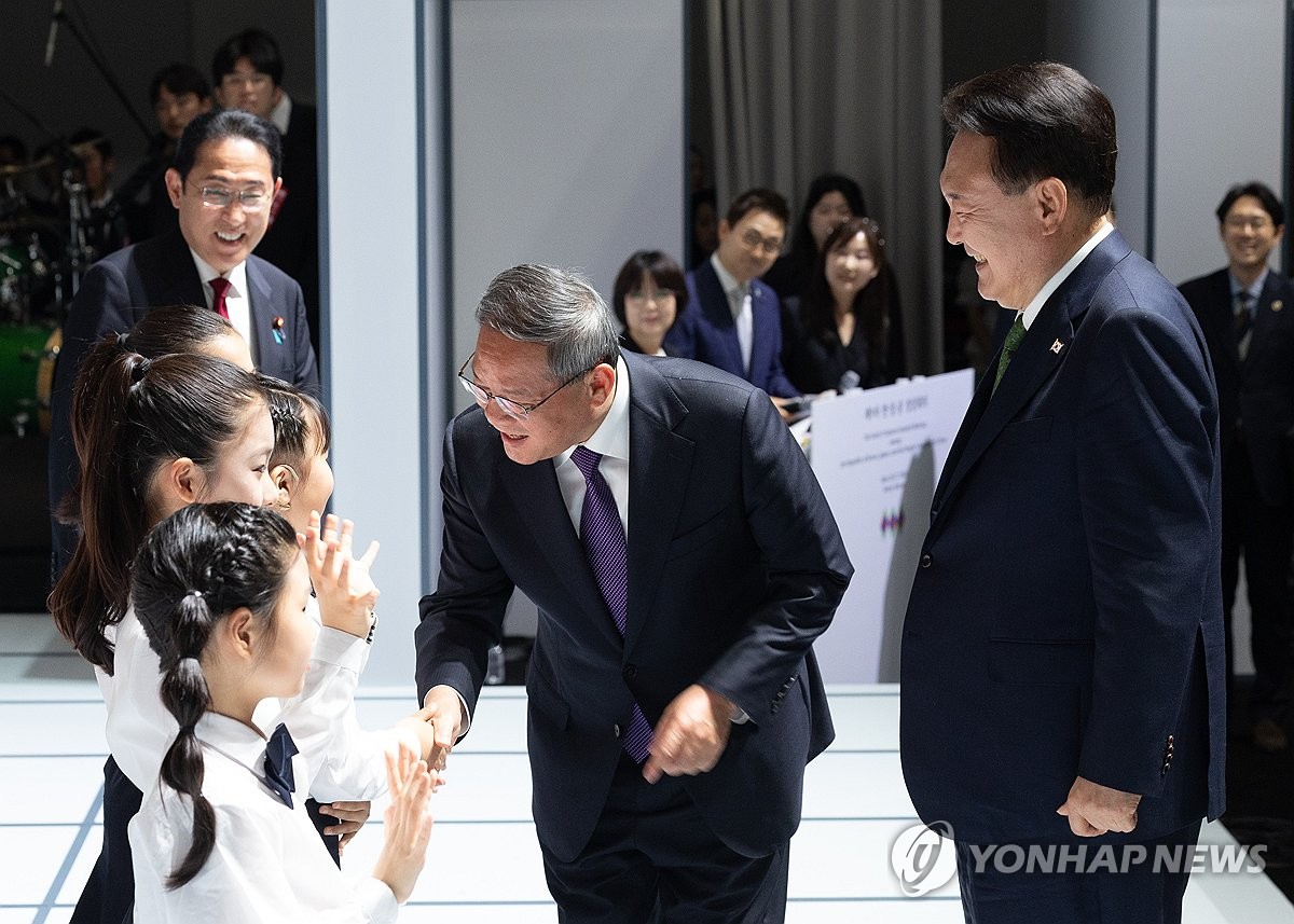 5月26日，在位于首尔三清洞的国立现代美术馆，中国国务院总理李强（右二）与韩中日三国儿童合唱团团员握手致意。 韩联社/总统室供图（图片严禁转载复制）